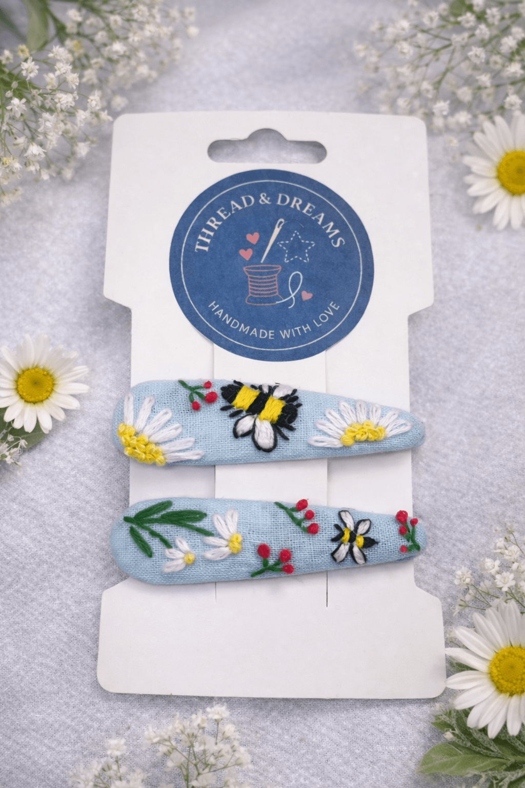 Handmade fabric hair clips featuring embroidered white daisies and a tiny hand-stitched bumblebee by Thread & Dreams.